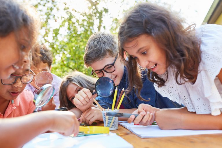 Group of school kids using a magnifier for a collaborative STEM classroom activity
